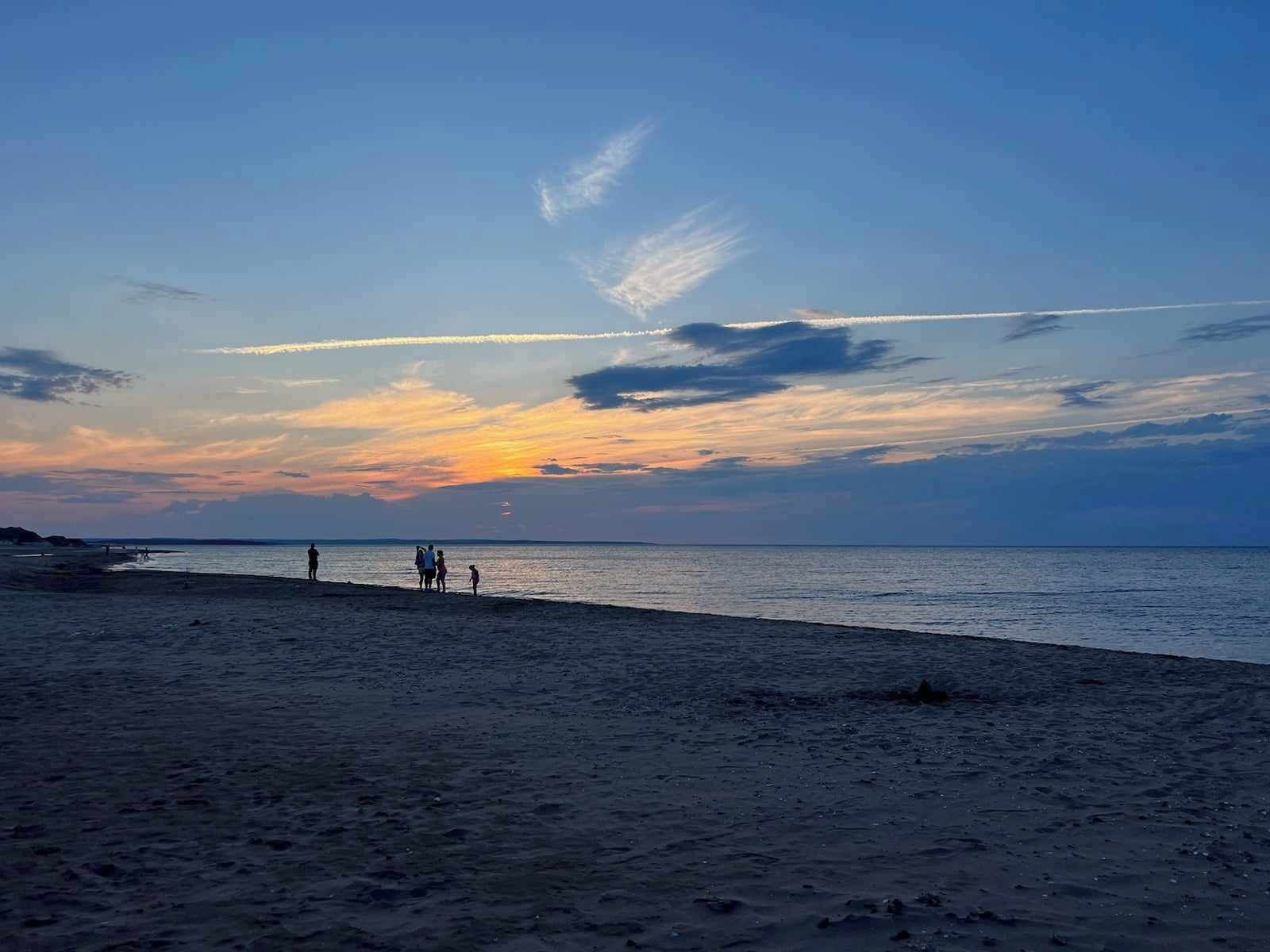 Una spiaggia al tramonto, mare calmo e alcune persone che passeggiano.