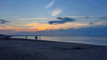 Una spiaggia al tramonto, mare calmo e alcune persone che passeggiano.