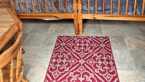 Una cama de madera con cabecera, dos lámparas de noche, una alfombra estampada y una silla de madera.