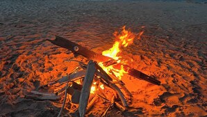 Una fogata sobre una playa arenosa, con el océano al fondo.