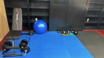 Une salle de sport équipée d’un tapis bleu, d’un banc de musculation, d’haltères, d’un ballon lesté et d’un support pour les exercices de squat.