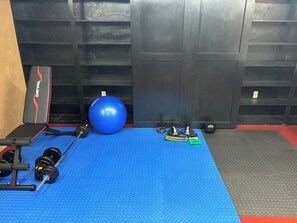 A gym with exercise equipment including a bench, dumbbells, a medicine ball, and resistance bands.
