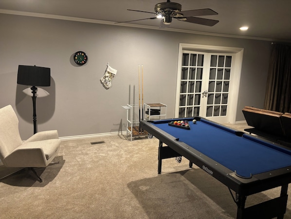 A pool table with balls, a chair, a lamp, a ceiling fan, and a door with glass panels.