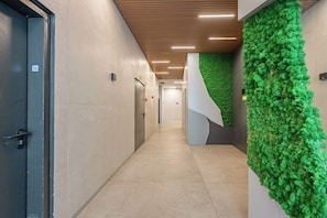 A hallway with a green wall feature, a door labeled '56', and a tiled floor. - Bright Stay • Private Skyline Balcony by SeaNRent (Tel-Aviv)