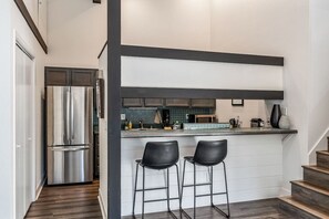 Une cuisine moderne dotée d’un coin bar, d’appareils électroménagers en acier inoxydable et d’un escalier menant à un autre niveau.