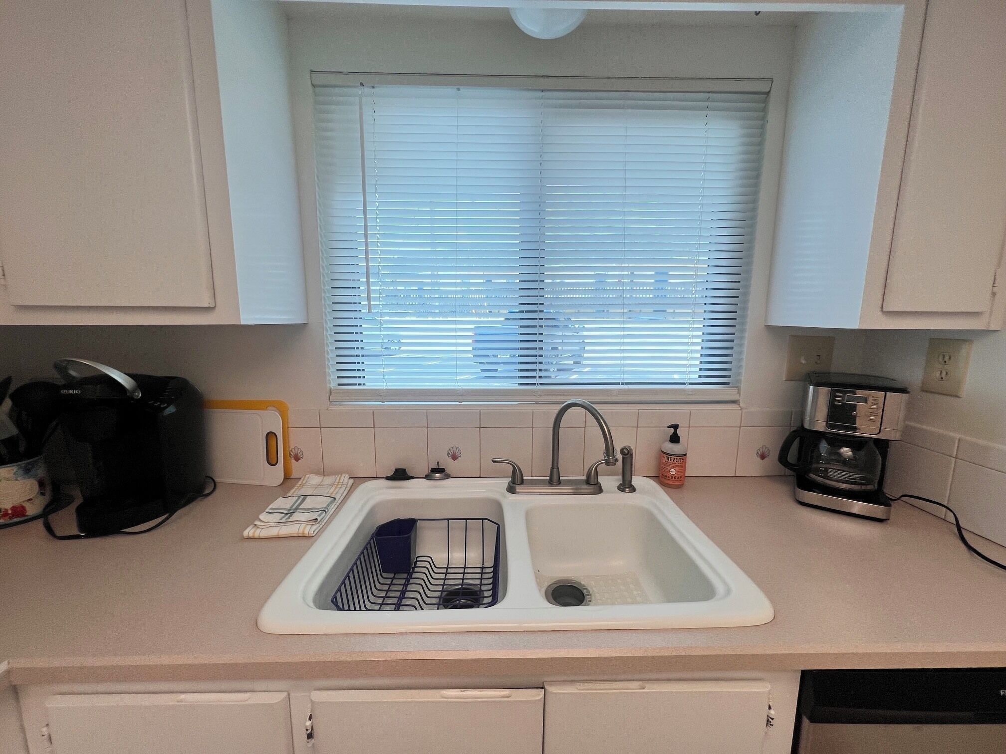 A kitchen with a sink, a coffee maker, and a window with blinds.