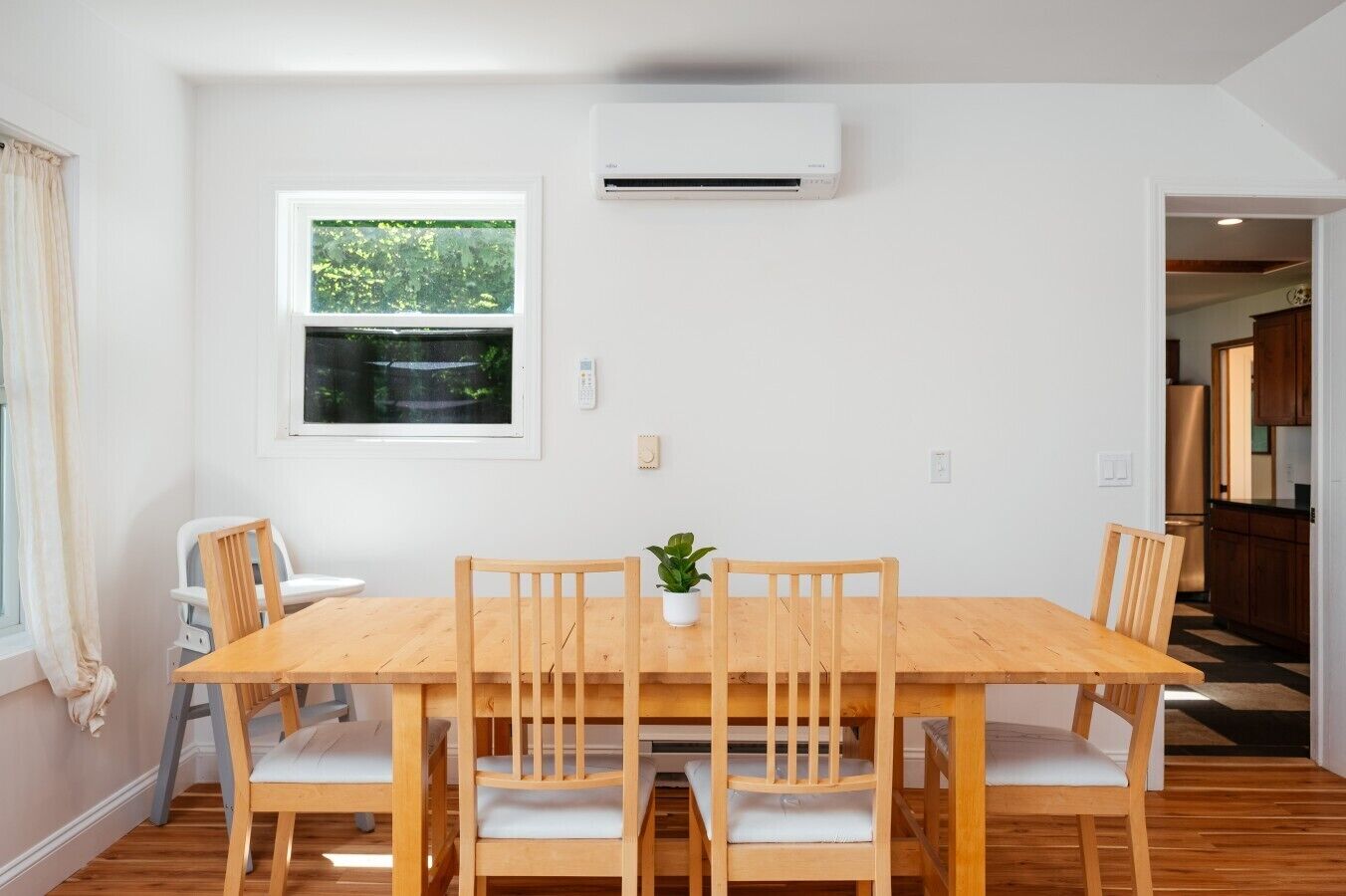 A dining area with a wooden table and chairs, a potted plant, and an air conditioning unit on the wall.