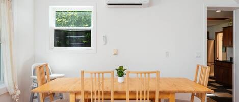A dining area with a wooden table and chairs, a potted plant, and an air conditioning unit on the wall.