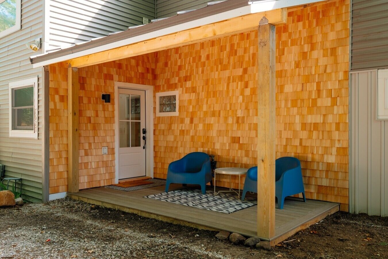 Covered entryway porch featuring cedar shingle walls, blue patio chairs, and front entry door.