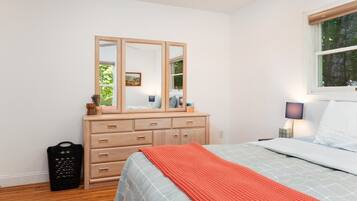 A bedroom with a bed, a dresser with a mirror, a window, and a nightstand with a lamp.