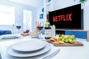 Ein Essbereich mit Tisch für zwei Personen, einer Weinflasche und einem Fernseher mit dem Netflix-Logo.