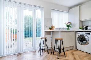 A modern kitchen with a washing machine, two stools, and a view through large sliding doors to an outdoor area. - Bold & Cosy 3BDR | Family Home | Parking | Wi-Fi (Tividale)