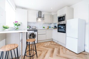 A modern kitchen with white cabinetry, a built-in washing machine, a refrigerator, and a herringbone wood floor. - Bold & Cosy 3BDR | Family Home | Parking | Wi-Fi (Tividale)