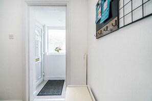 A hallway with a door leading to a room, a small window with a view, and a wall-mounted shelf with items. - Bold & Cosy 3BDR | Family Home | Parking | Wi-Fi (Tividale)