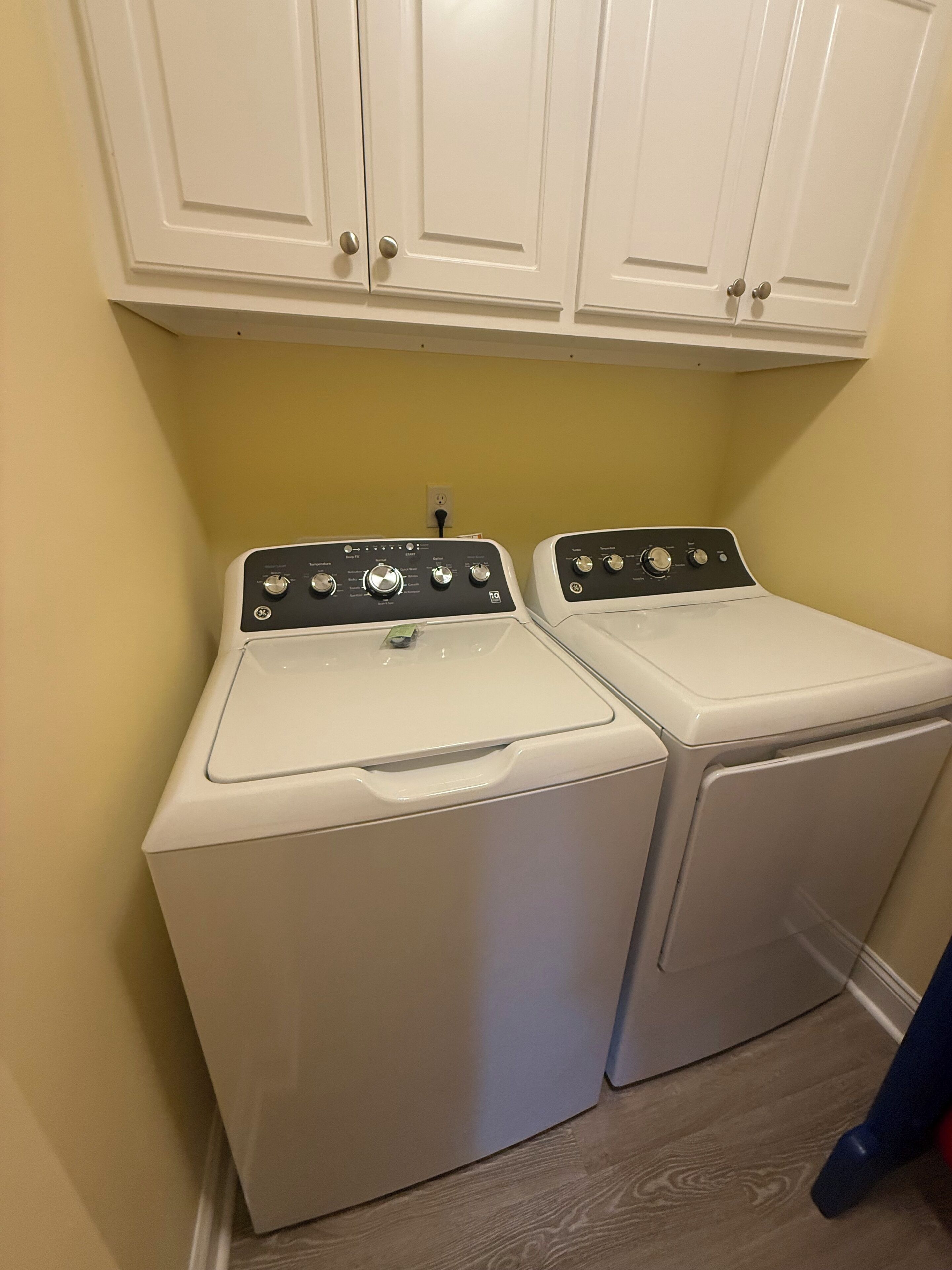 A laundry room with two front-loading washing machines and white cabinets above.