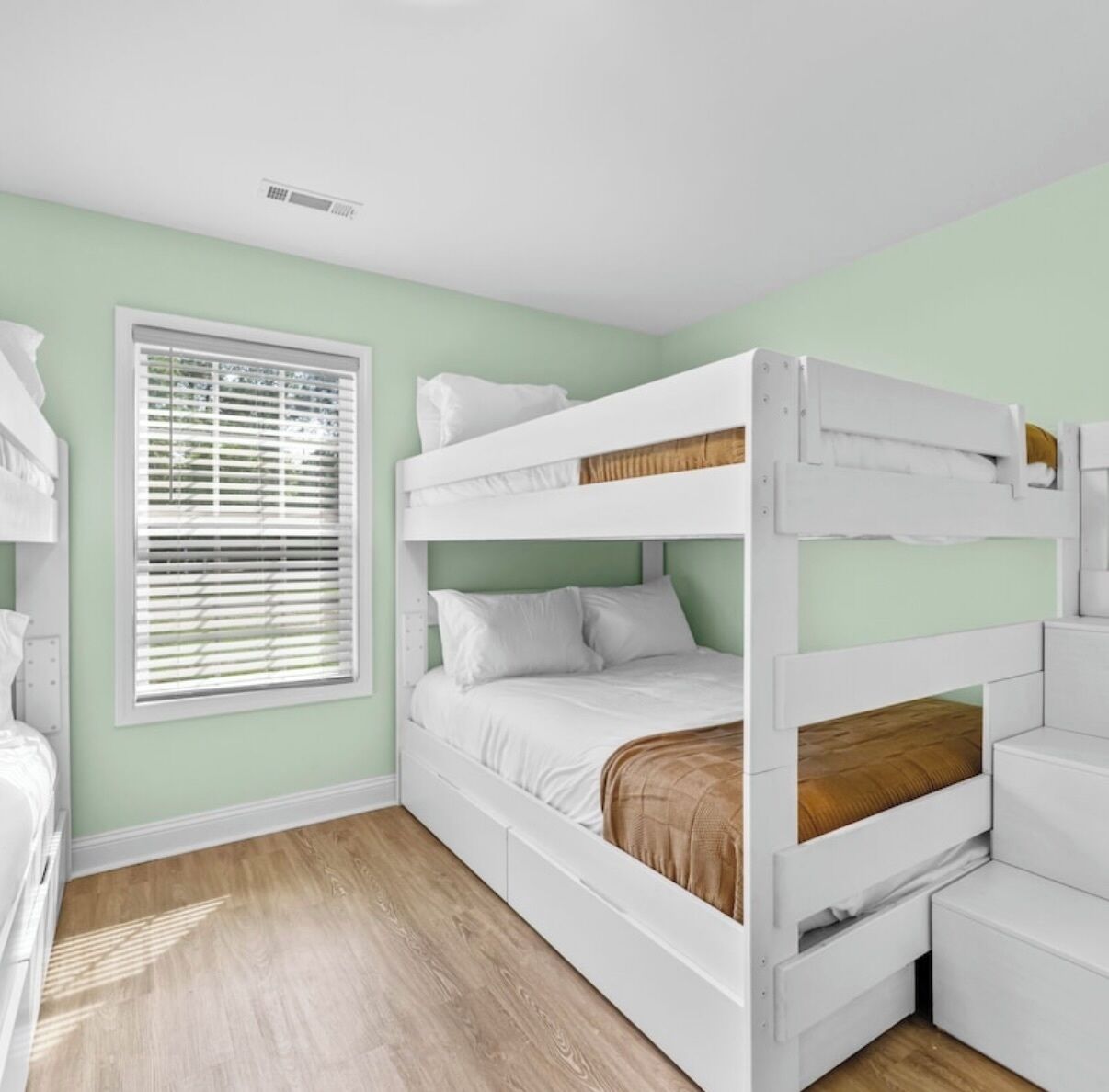 A bunk bed with white bedding, a window with blinds, and a wooden floor.