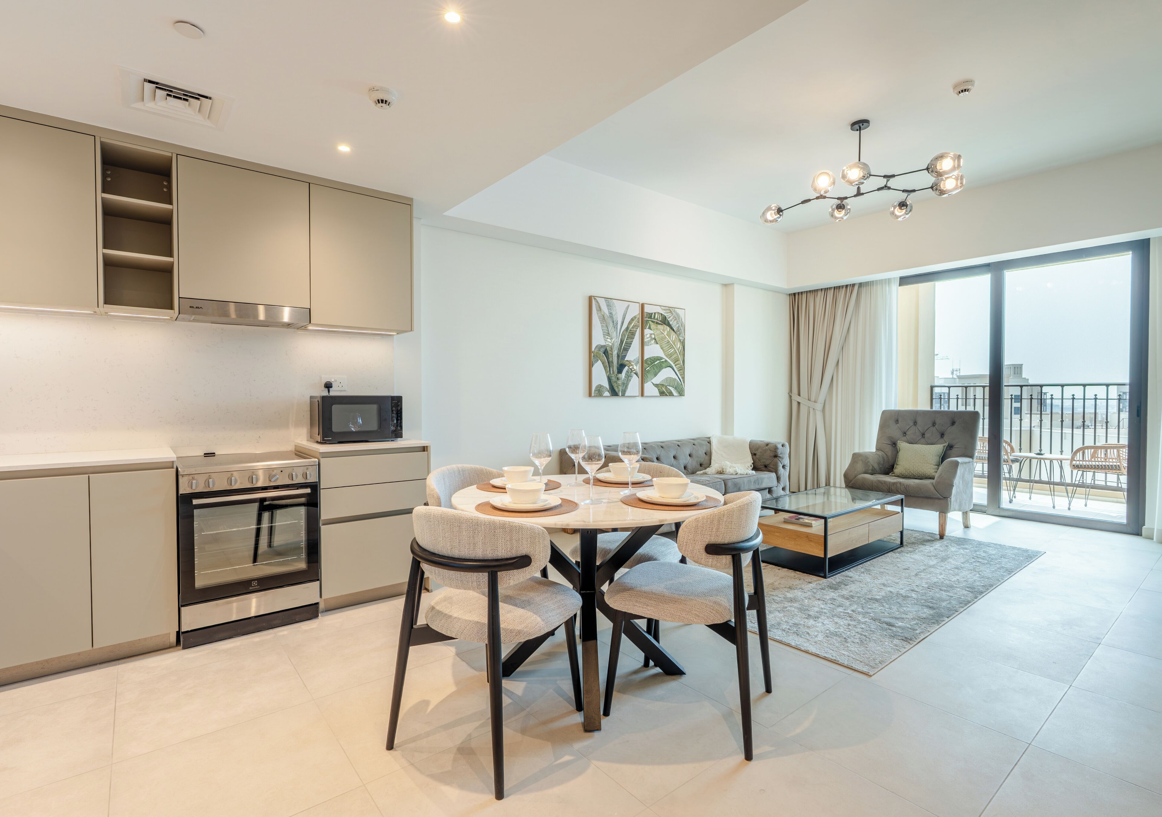 A modern kitchen with built-in appliances, a dining area with a round table and chairs, and a balcony with a view.