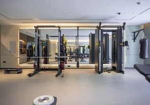 A modern gym with weightlifting equipment, a punching bag, and a mirror reflecting the space. - 1BR Umm Suqiem Apartment w/ Burj Al Arab Pool View, Steps to Kite Beach (Dubai)