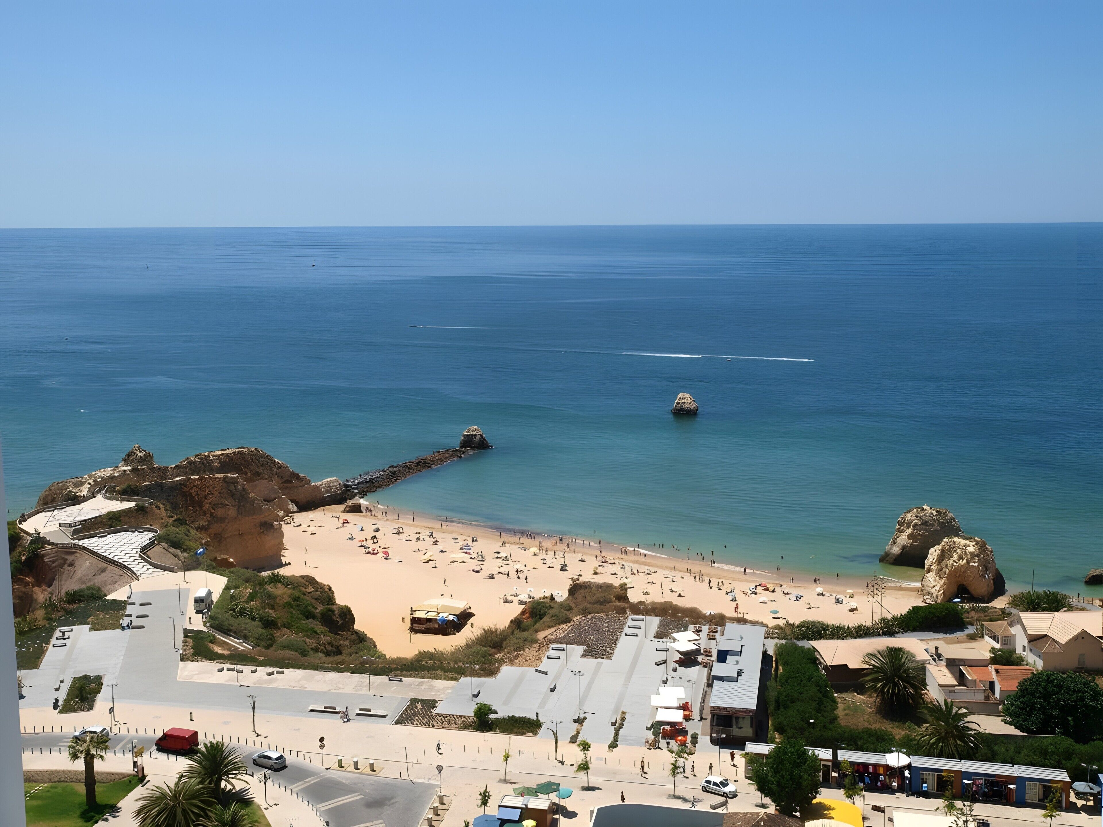 A coastal town with a beach, rocky formations, and a clear sky.