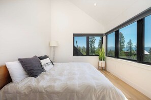 A bedroom with a large bed, a potted plant, and a view of trees through large windows. - Ridgeline Retreat | Modern 4BR, Big Mountain Views (Tabernash)