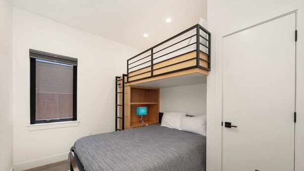 A single bedroom with a bunk bed, a bedside lamp, a window with blinds, and a door. - Ridgeline Retreat | Modern 4BR, Big Mountain Views (Tabernash)