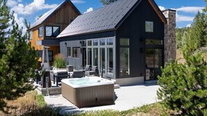 A modern two-story house with a large glass door entrance, a hot tub, and outdoor seating. - Ridgeline Retreat | Modern 4BR, Big Mountain Views (Tabernash)