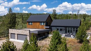 A modern two-story house with a stone foundation, a wooden cabin, and a large garage. - Ridgeline Retreat | Modern 4BR, Big Mountain Views (Tabernash)