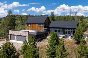 A modern two-story house with a stone foundation, a wooden cabin, and a large garage.