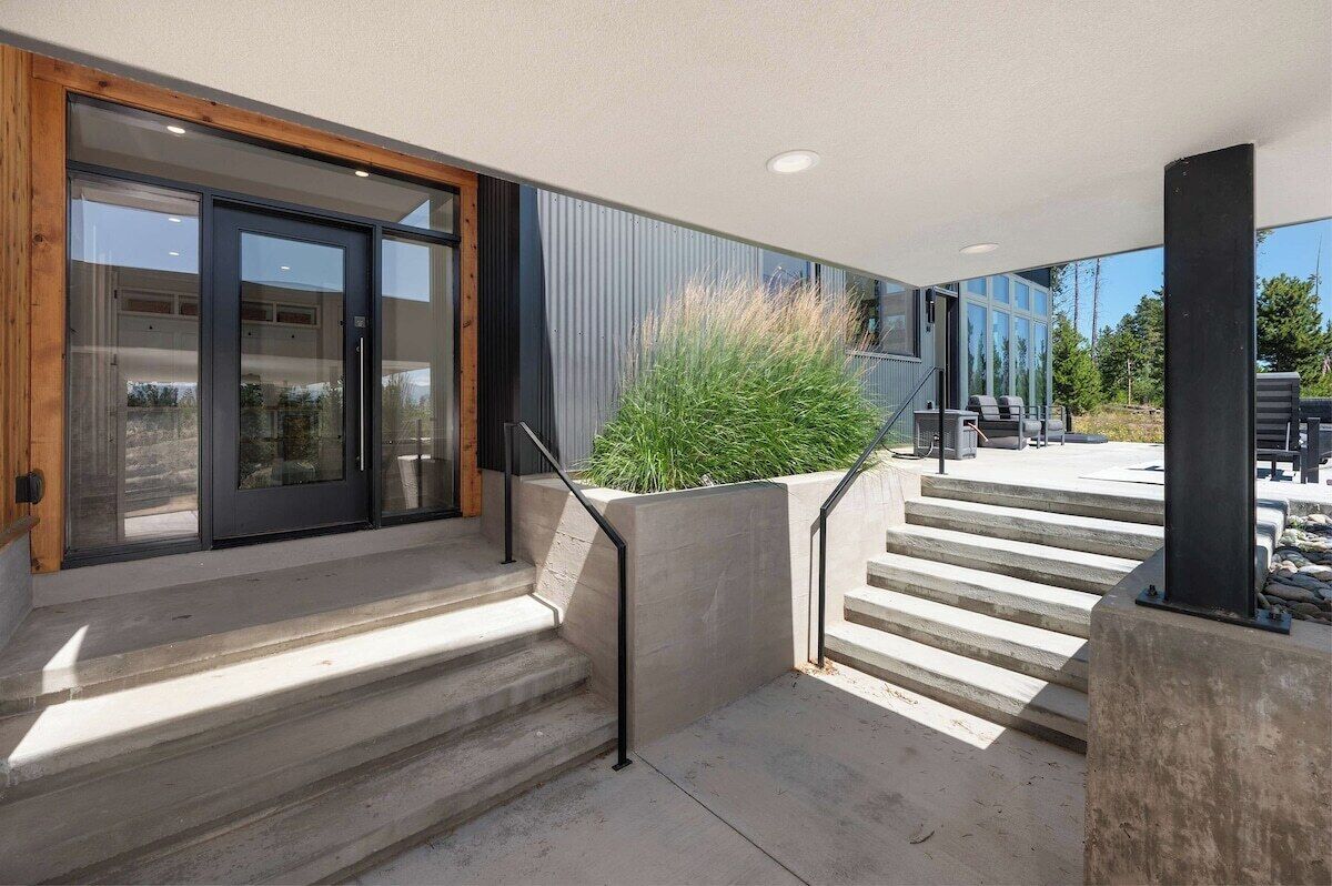 A modern building entrance with a glass door, concrete steps, and a metal railing.