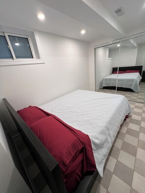 A bedroom with a bed, a mirror, and a window. - Spacious 2 Bed Basement Apartment Fully Furnished, Separate Entrance (Toronto)
