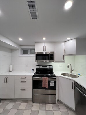 A modern kitchen with stainless steel appliances, white cabinetry, and a tiled floor. - Spacious 2 Bed Basement Apartment Fully Furnished, Separate Entrance (Toronto)