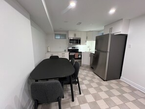 A compact kitchen with a dining table, chairs, a refrigerator, and a microwave. - Spacious 2 Bed Basement Apartment Fully Furnished, Separate Entrance (Toronto)