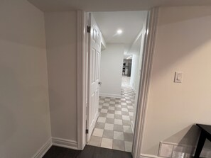 A hallway with a checkered floor, white walls, and a door leading to a kitchen area. - Spacious 2 Bed Basement Apartment Fully Furnished, Separate Entrance (Toronto)
