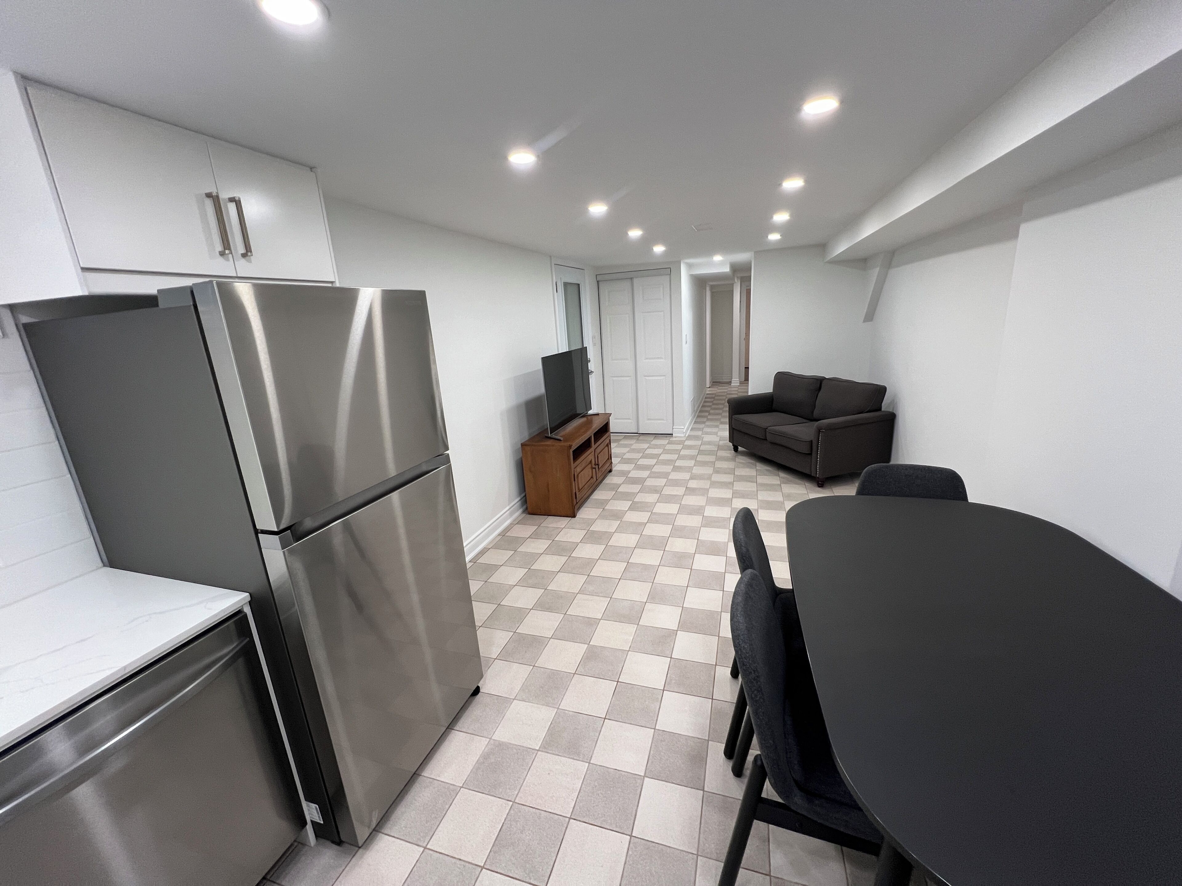 A compact kitchen with a refrigerator, a wooden cabinet, and a television on a stand.