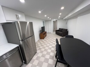 A compact kitchen with a refrigerator, a wooden cabinet, and a television on a stand. - Spacious 2 Bed Basement Apartment Fully Furnished, Separate Entrance (Toronto)