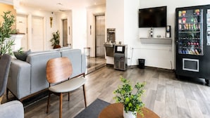 Un hall d’hôtel moderne avec un canapé, des fauteuils, une machine à café, un téléviseur et un distributeur automatique.