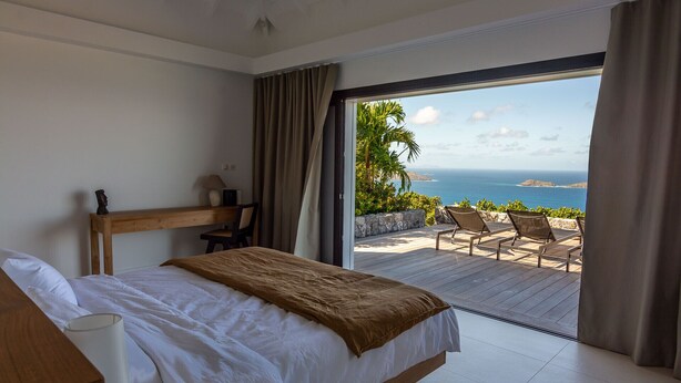 Een slaapkamer met een bed, een bureau en uitzicht op zee.