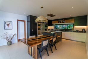 A modern kitchen with a central island, built-in appliances, and a large window overlooking greenery. - Villa Mao (2 bedrooms) (Saint Barthélemy)