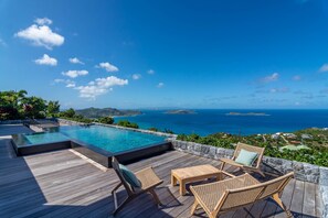A rooftop infinity pool with wooden deck and wicker furniture, overlooking a coastal landscape with clear skies. - Villa Mao (2 bedrooms) (Saint Barthélemy)