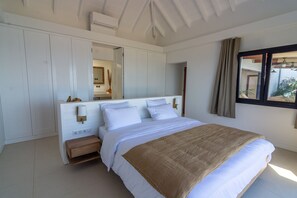 A bedroom with a large bed, a bedside table, a mirror, and a window with curtains. - Villa Mao (2 bedrooms) (Saint Barthélemy)