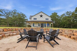 A modern house with a star on the roof, surrounded by a stone wall and outdoor seating with Adirondack chairs. - Quiet Pond Retreat - Minutes from A&M - Sleeps 12 (College Station)