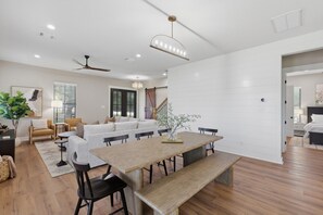 A modern living room with a wooden dining table, black chairs, a sofa, and a ceiling fan. - Quiet Pond Retreat - Minutes from A&M - Sleeps 12 (College Station)