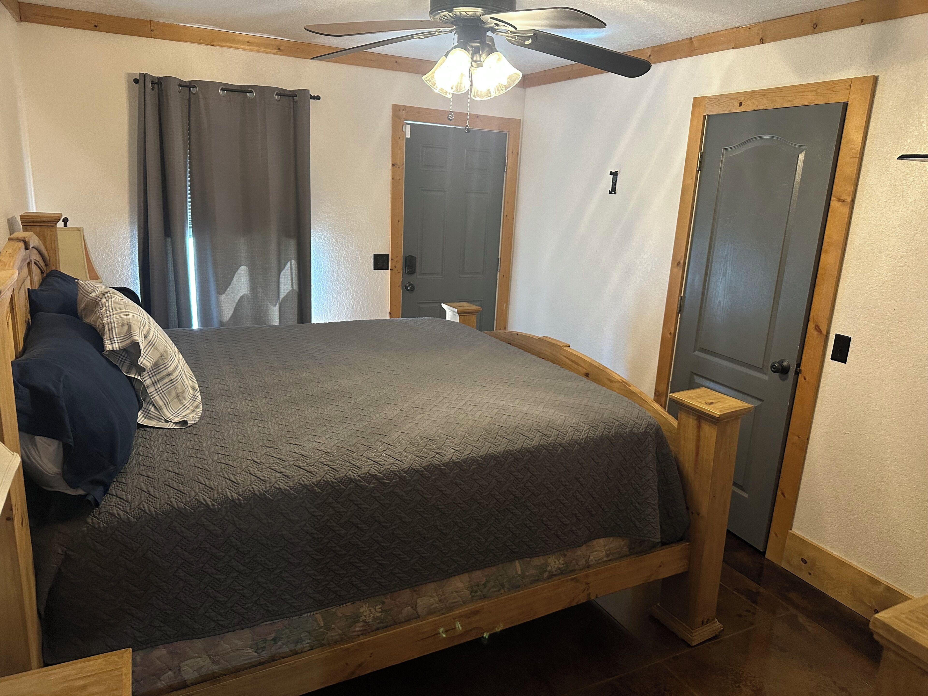 Une chambre à coucher avec un lit, une tête de lit en bois, un ventilateur de plafond et deux portes.