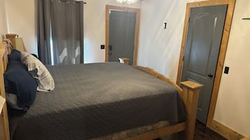 Une chambre à coucher avec un lit, une tête de lit en bois, un ventilateur de plafond et deux portes.