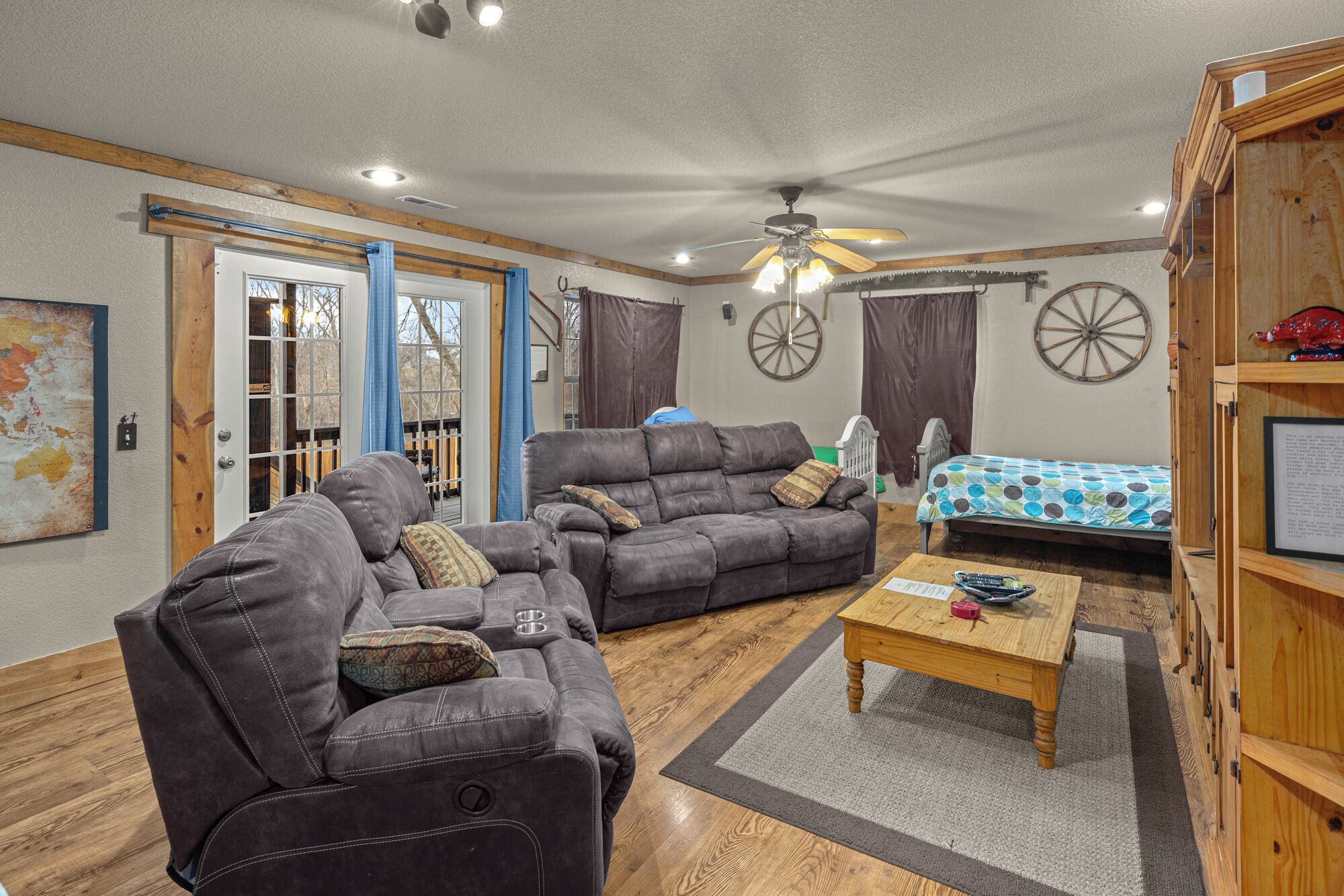 A furnished living room with a sofa set, a wooden coffee table, and a bed with a patterned bedspread.