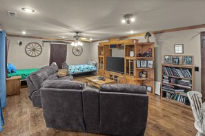 Ein möbliertes Wohnzimmer mit einer Couch, einem Fernseher, einem Bücherregal und einem Deckenventilator.