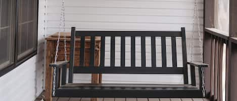 Une véranda en bois avec un banc noir, un revêtement extérieur blanc et une table en bois.