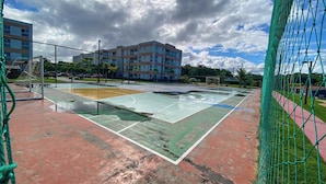 A basketball court with a net, a goalpost, and a building in the background. - Muro Alto Condomínio Clube por YOLO (Ipojuca)