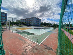 A basketball court with a net, a goalpost, and a building in the background. - Muro Alto Condomínio Clube por YOLO (Ipojuca)