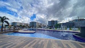 A swimming pool area with a wooden deck, lounge chairs, and a palm tree. - Muro Alto Condomínio Clube por YOLO (Ipojuca)
